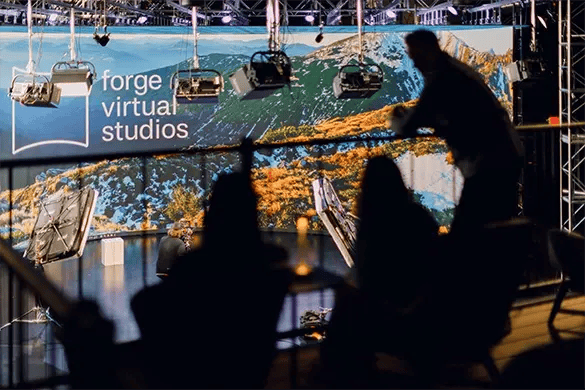 Three filmmakers overlook a virtual production LED stage from a client lounge space