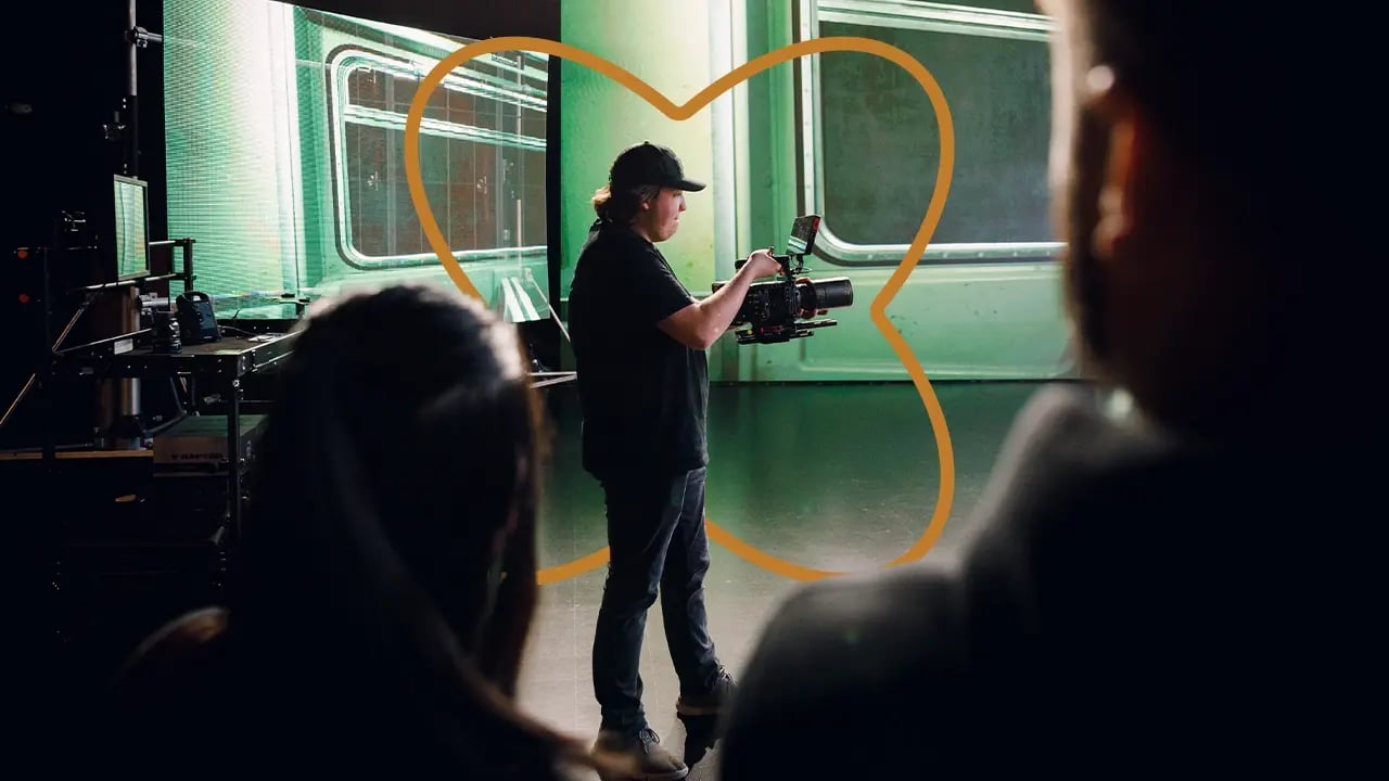 A cinematographer operates a RED cinema camera on a virtual production stage as crew members watch